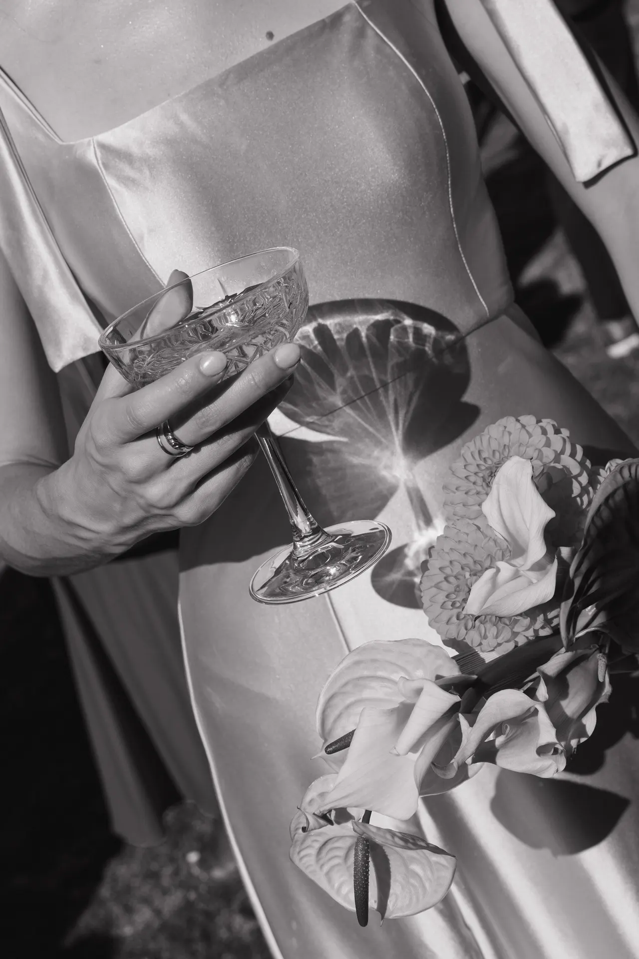 Black-and-white detail of a hand holding a cocktail beside wedding flowers