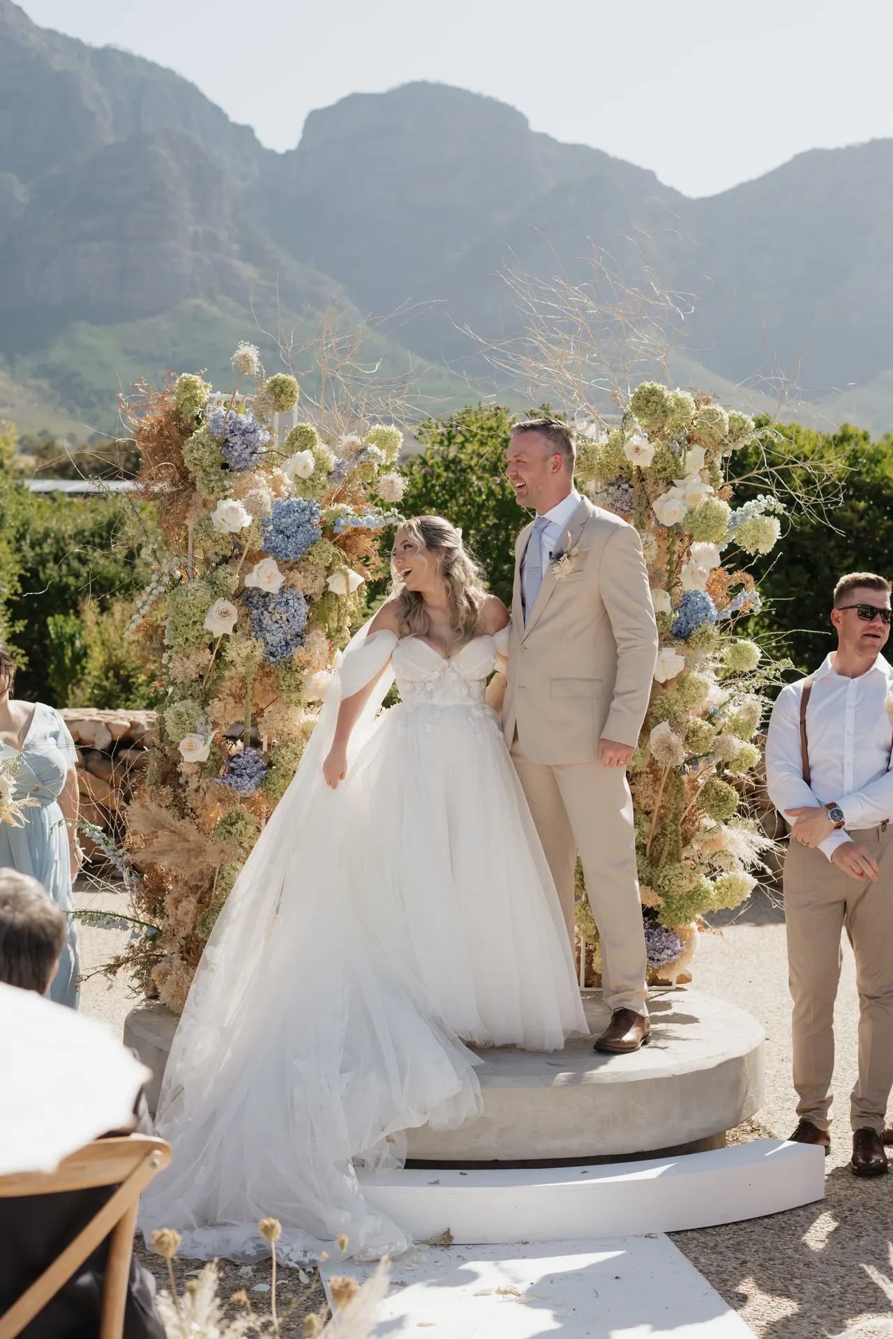 Couple at their ceremony beneath an arch of hydrangeas, guests looking on
