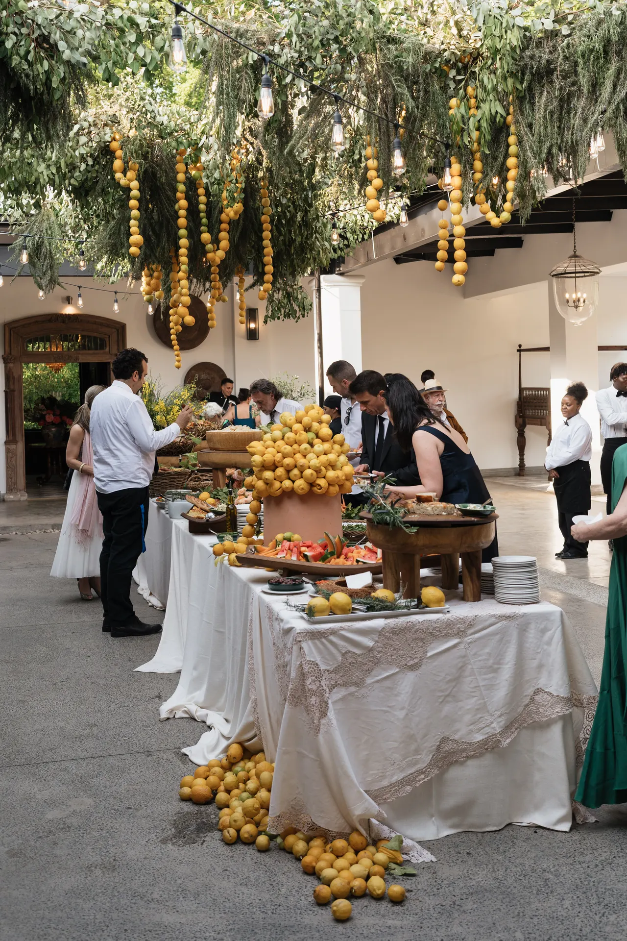 Abundant outdoor feast table piled with lemons beneath hanging citrus