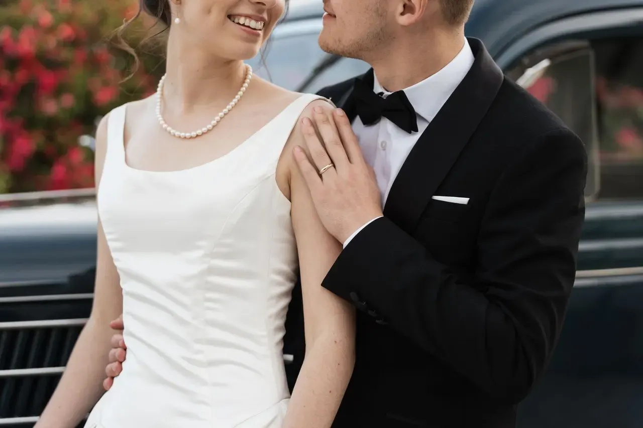 Close detail of the couple: pearls, satin and a black tuxedo