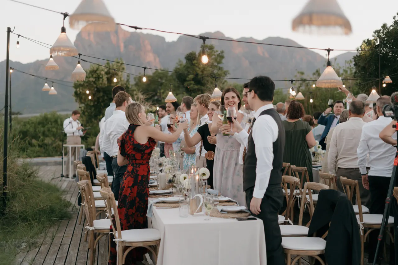 Wedding guests raising a toast at long reception tables under string lights